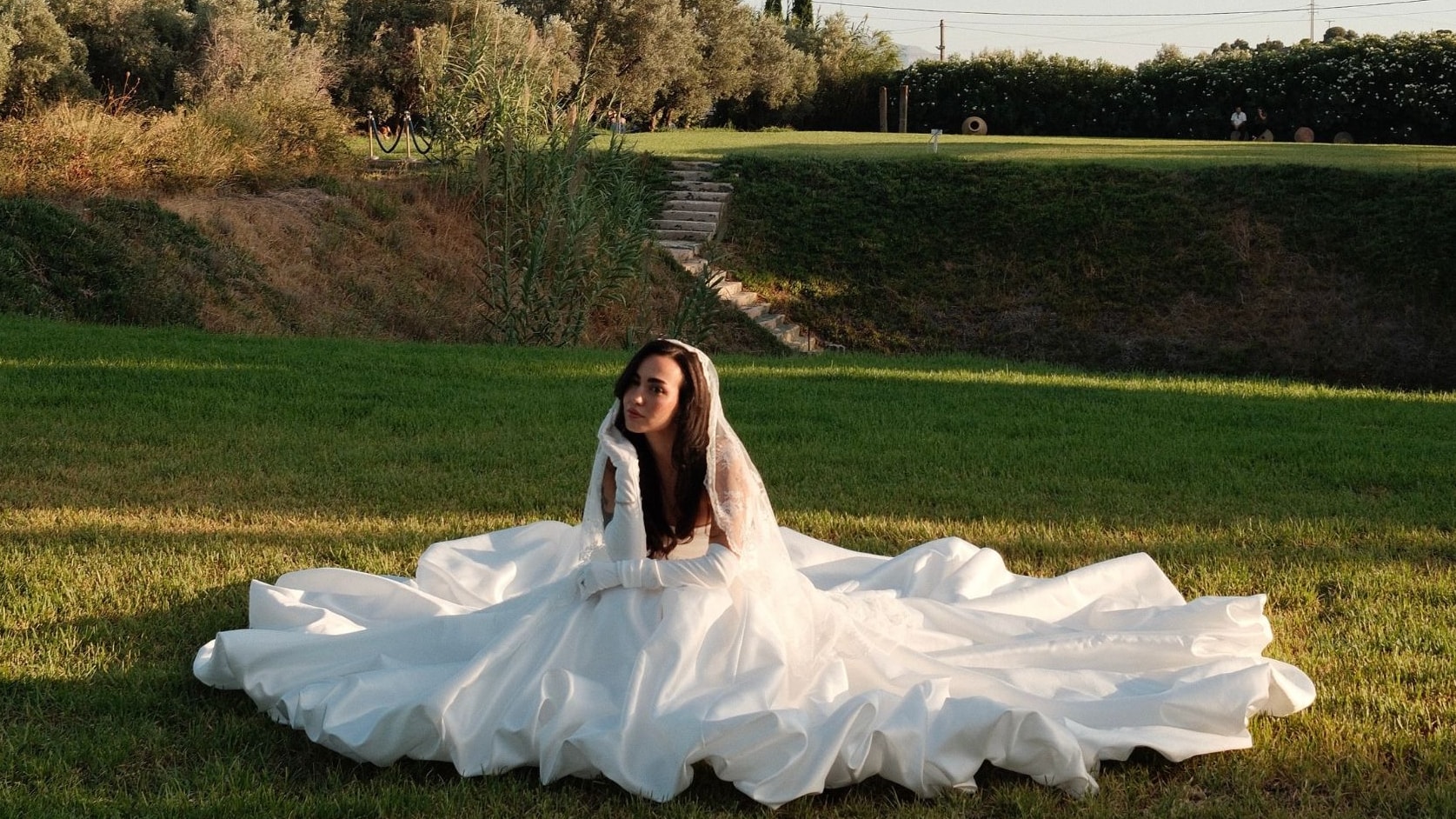 Bride in her gown seated on the grass at golden hour